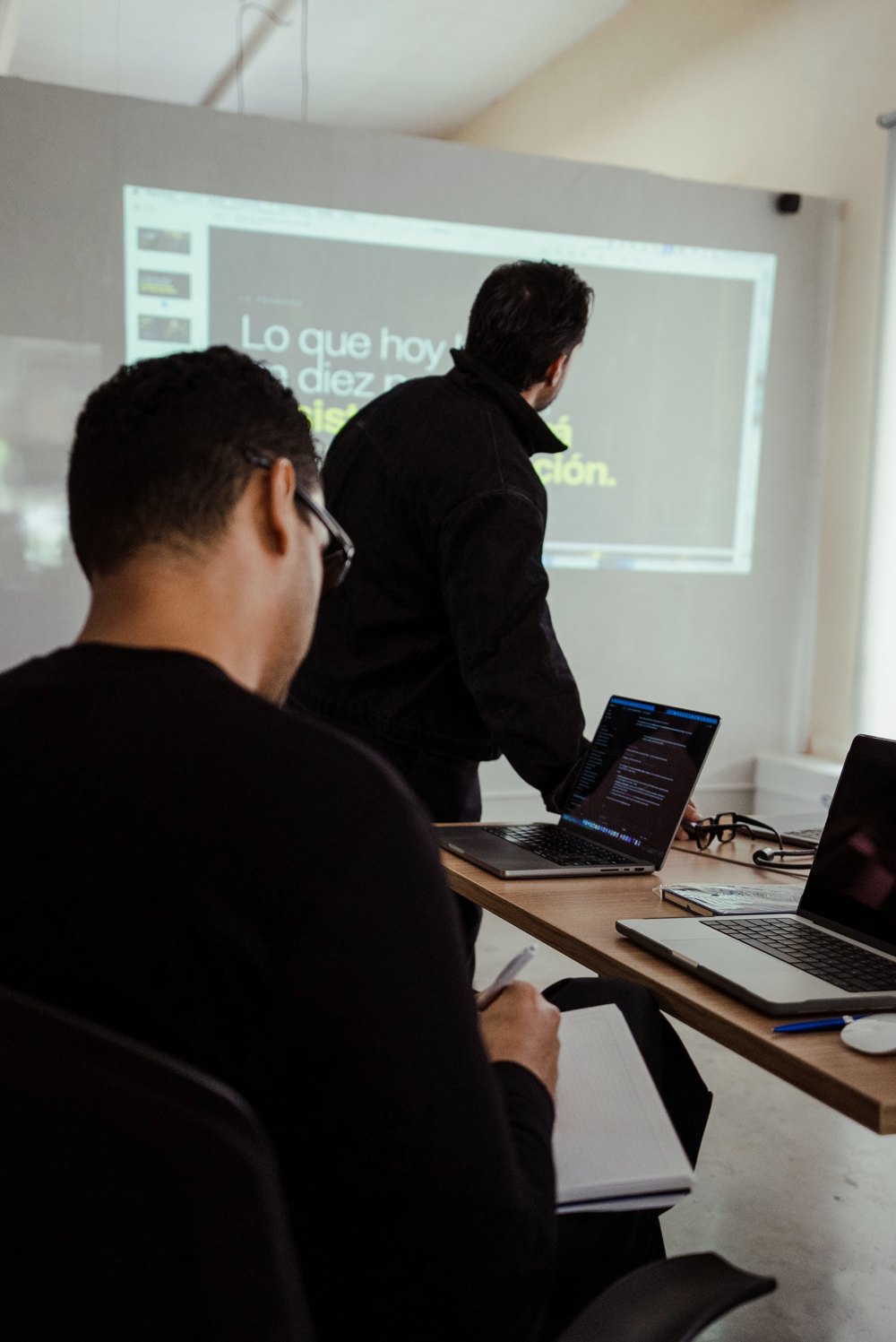 Un equipo trabaja en sus portátiles con la proyección al fondo